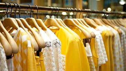 Стелаж за дрехи с разнообразни жълти ризи на закачалки.